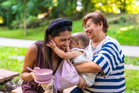 Latin family enjoying time together in park, grandmother holding granddaughter while mother is