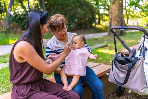 Latin family enjoying a sunny day outdoors, with grandmother and mother lovingly feeding a baby
