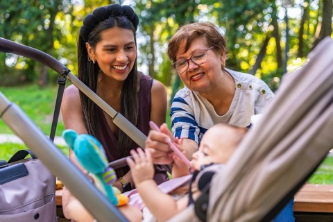 Grandmother lovingly feeding baby girl with a spoon while mother watches from the stroller in a