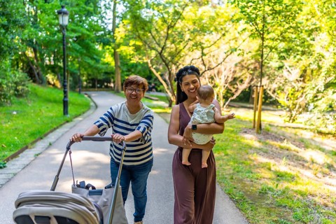 Happy latin family walking in a park, grandmother pushing a stroller and mother holding her baby