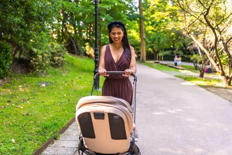 Latin mother pushing a stroller with a happy baby inside, enjoying a sunny day while walking