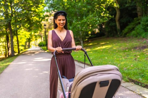 Latin mother enjoying a walk in the park, pushing a stroller with her baby inside, on a sunny day
