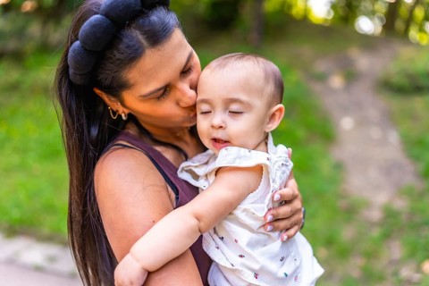 Young latin mother kissing her baby daughter while holding her lovingly in her arms, surrounded by