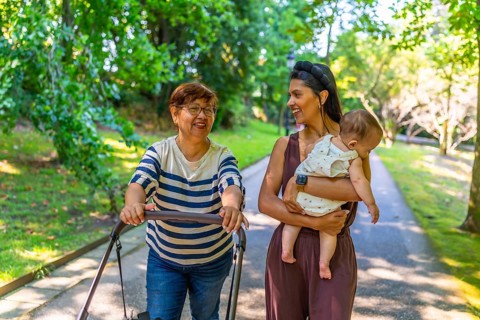 Grandmother, mother, and baby girl enjoying a sunny day at the park, pushing a stroller and