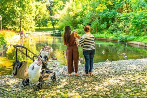 Mother, grandmother and baby girl enjoying a sunny day by the pond, watching ducks swim in a park