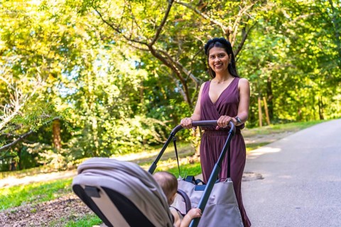 Latin mother enjoying a sunny summer day while walking in the park with her baby in a stroller,
