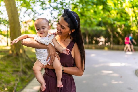 Happy latin mother holding and playing with her baby daughter in a park, enjoying a sunny day