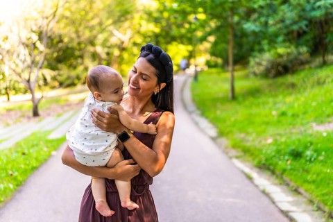 Latin mother holding her baby daughter, smiling and enjoying a walk in a park during a sunny day