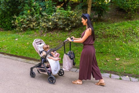 Young mother enjoying a sunny day in the park, happily pushing her baby girl in a stroller along a