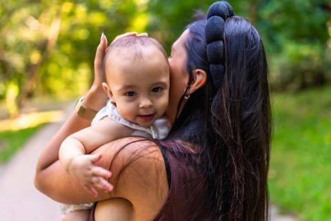 Mother cuddling her baby girl while strolling through a park, savoring a sunny day filled with