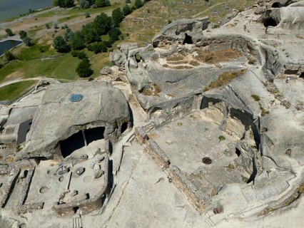 Cave complex with ruins near a river, surrounded by lush nature and rocks, aerial view, cave town
