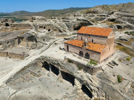 Fascinating ruins of Uplistsikhe with orange tiled roofs in the middle of a rocky landscape, aerial