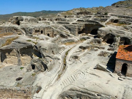 Ancient cave town with weathered sandstone structures and old paths under a blue sky, aerial view,
