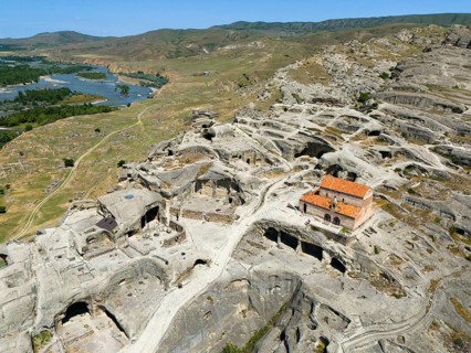 Ruins of the ancient cave city of Uplistsikhe overlooking a wide river and hilly landscape, aerial