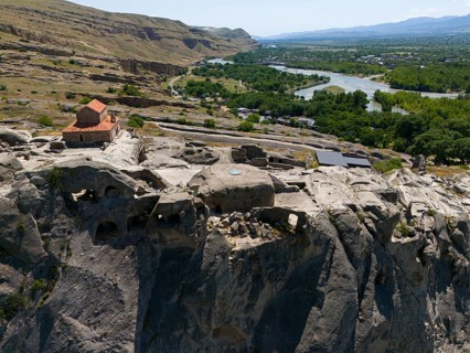 Historic church on rocky cliff with panoramic view of river and green landscape, aerial view, cave