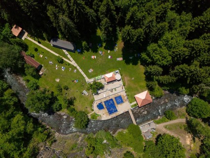 Aerial view of a forest area with swimming pool, river and surrounding buildings, surrounded by