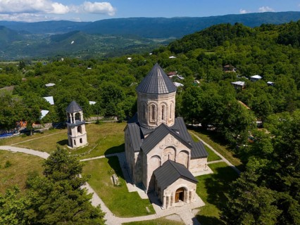 Traditional church surrounded by green landscape and hilly surroundings under blue sky, aerial