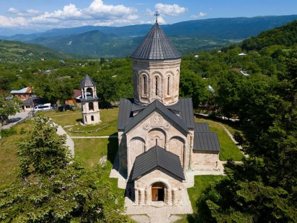 Historic church in a green mountain landscape under a blue sky with clouds, aerial view,