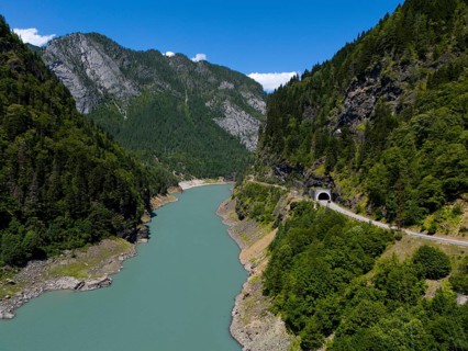A turquoise-coloured river flows through a wooded valley with mountains and a tunnel in the