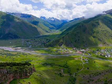 Green valley with river and village, surrounded by high mountains and cloudy sky, aerial view, view