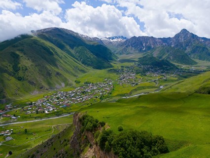Panoramic view of green valley with village and mountains under a cloudy sky, aerial view, view