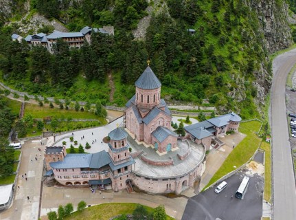Large red brick church embedded in a wooded mountain landscape under a slightly cloudy sky, aerial