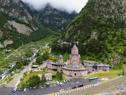 A large red brick church lies picturesquely in a mountainous valley under clouds, aerial view,