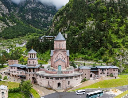 Impressive red brick church surrounded by forested mountains under a cloudy sky, aerial view,