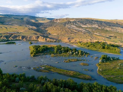 A picturesque river landscape with green islands and surrounding hills under a blue sky, aerial