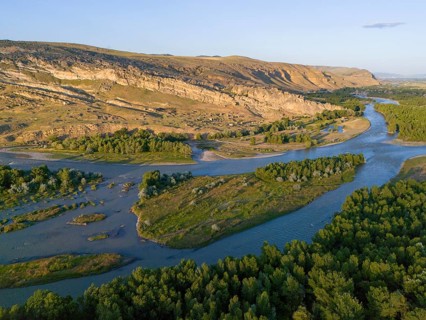 Extensive river landscape with green islands and rocky cliffs, framed by forest areas under a clear