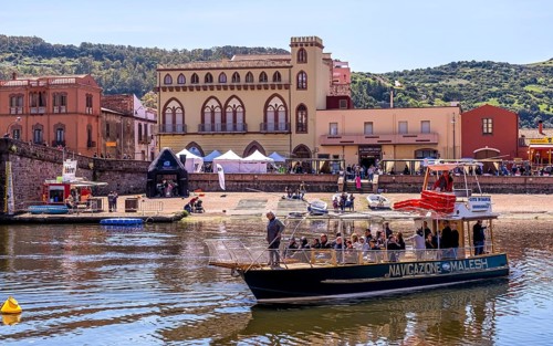 Sardinia, boats in the river Temo and houses on the promenade, guests at the restaurants with