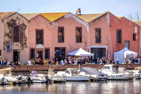 Sardinia, boats in the river Temo and houses on the promenade, guests at the restaurants with