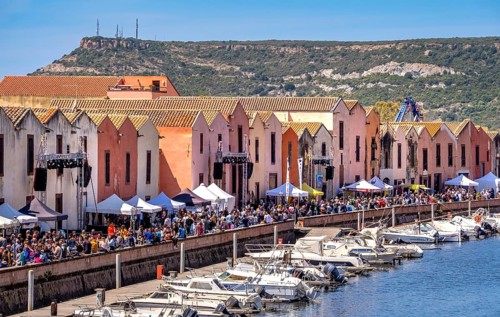 Sardinia, boats in the river Temo and houses on the promenade, guests at the restaurants with