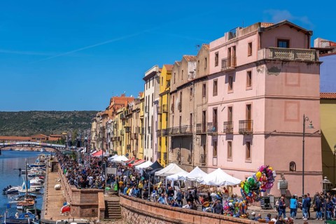 Sardinia, boats in the river Temo and houses on the promenade, guests at the restaurants with