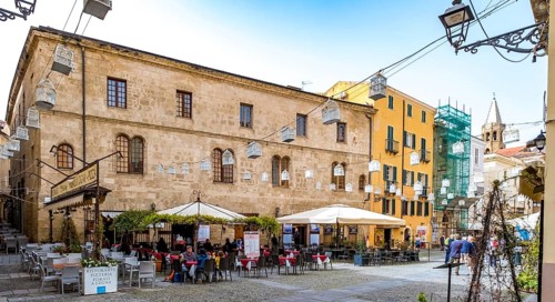 Sardinia, tourist tour group in the old town with sandstone-coloured palazzi, birdcage from house