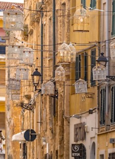 Sardinia, birdcage with light bulbs on power lines between houses above the alleyway, old town,