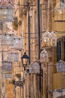 Sardinia, birdcage with light bulbs on power lines between houses above the alleyway, old town,