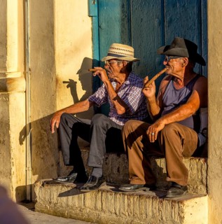 Two old Cubans smoking cigars and sitting on a staircase in the warm light of the sunset, Trinidad,