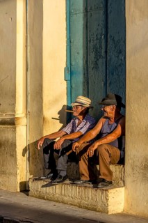 Two old Cubans smoking cigars and sitting on a staircase in the warm light of the sunset, Trinidad,