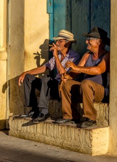Two old Cubans smoking cigars and sitting on a staircase in the warm light of the sunset, Trinidad,
