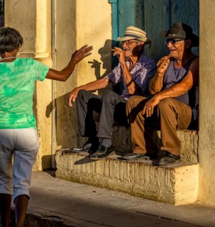Two old Cubans smoke cigars and sit on a staircase in the warm light of the sunset, they greet a