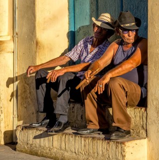Two old Cubans smoking cigars and sitting on a staircase in the warm light of the sunset, Trinidad,