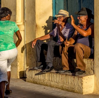 Two old Cubans smoke cigars and sit on a staircase in the warm light of the sunset, they greet a
