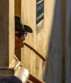 An old Cuban smokes a cigar and sits on a staircase in the warm light of the sunset, Trinidad,