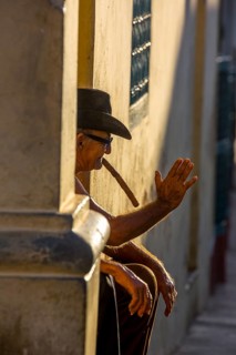 An old Cuban smokes a cigar and sits on a staircase in the warm light of the sunset, Trinidad,