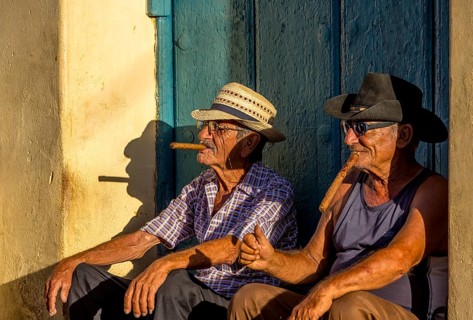 An old Cuban smokes a cigar and sits on a staircase in the warm light of the sunset, Trinidad,