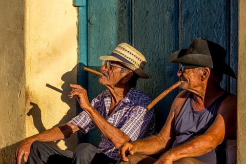 Two old Cubans smoking cigars and sitting on a staircase in the warm light of the sunset, Trinidad,