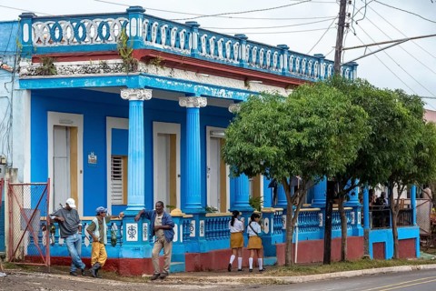Typical Cuban blue house with columns, workers and girls in school uniform, Viñales, Cuba, Pinar