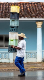 Cuban man with hat carrying and balancing crates of drinks across a street in Vinales, Viñales,