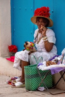 Old Cuban woman smokes a Cuban cigar on the street and posts with her cat for the tourists, La